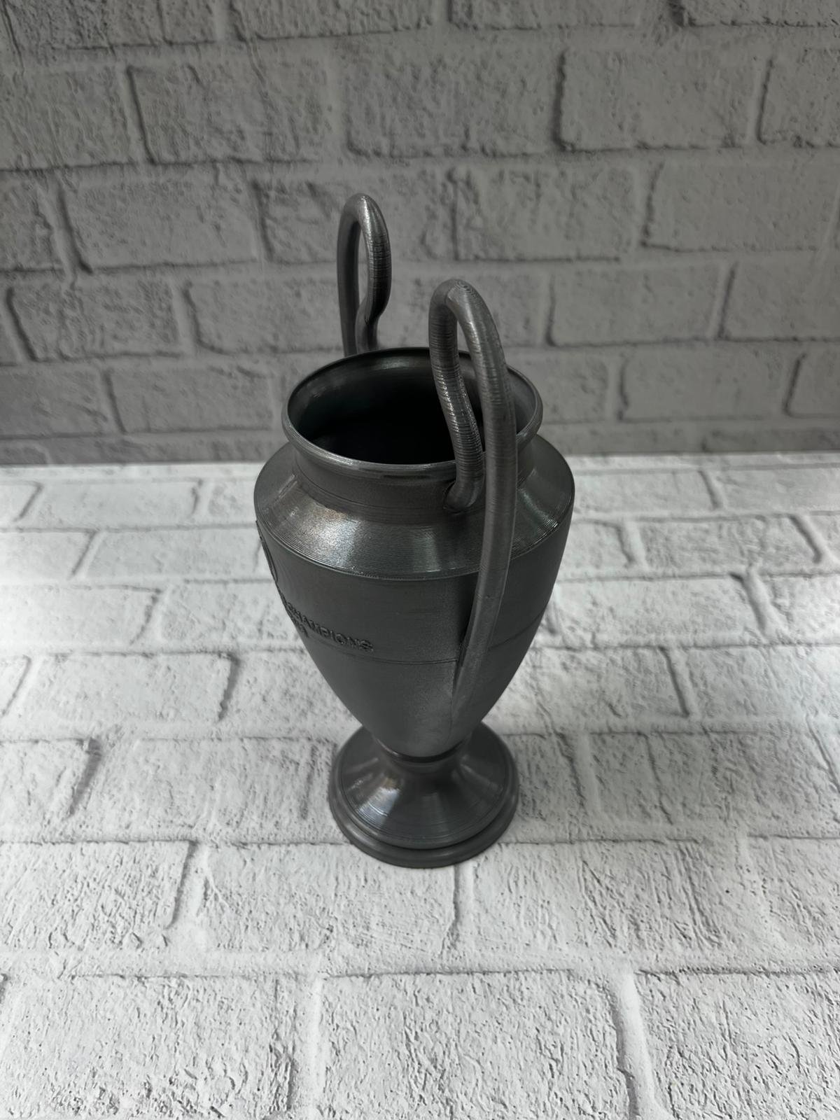 WhatsApp Image 2025 12 11 At 12.17.06 1 700x933 Füme Şampiyonlar Kupası 25cm Modern Dekor Ödül Biblo najmaddin.com UEFA Şampiyonlar Ligi kupasından ilham alınarak tasarlanmış şık ve premium bir dekoratif objedir. Mat füme tonu ve detaylı gövde yapısı ile spor temalı koleksiyonlarında özel bir yere sahip olur. Hafif fakat dengeli yapısıyla masa